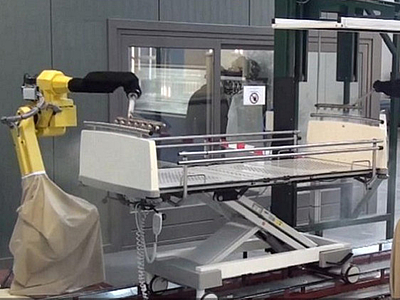 Photo: zwei Roboterarme reinigen ein Bettgestell 