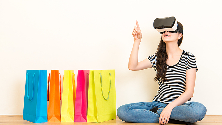 Photo: Frau mit VR Brille zeigt auf was sie kaufen möchte. Seitlich stehen Einkaufstüten