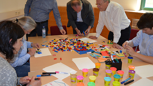 Photo: Seminarteilnehmer arbeiten an einem Tisch eine Aufgabe mit Legosteinen aus