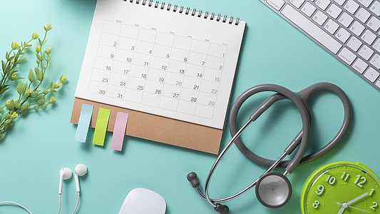 Photo: Tastatur, Kalender, Wecker und Stethoskop auf einem Tisch