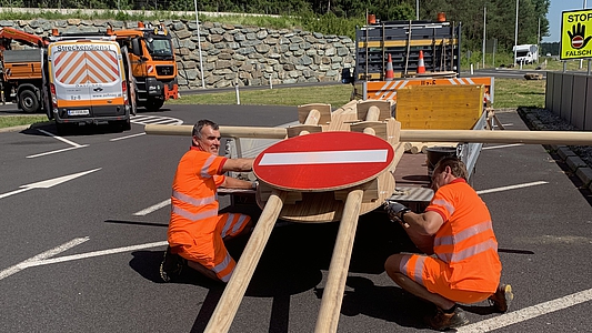 Foto: Zwei Mitarbeiter der Asfinag arbeiten an einem Stopschild aus Holz 