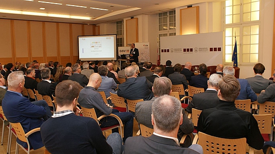 Photo: Teilnehmer der Veranstaltung im Publikum hören eine Präsentation 