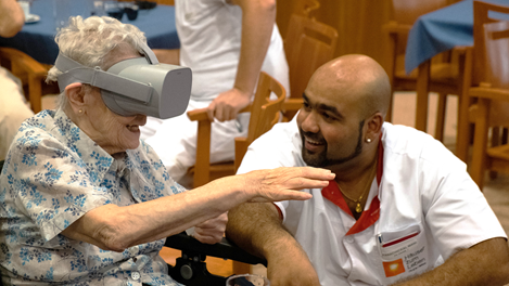Dame mit VR Brille lächelt, daneben sitzt ein Pfleger der sich freut 