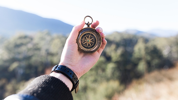 Photo: Hand hält einen Kompass, im Hindergund Natur