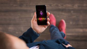 Photo: Eine Person hält ein Handy in der Hand, auf dem eine Sprachassistenten-App aktiviert ist